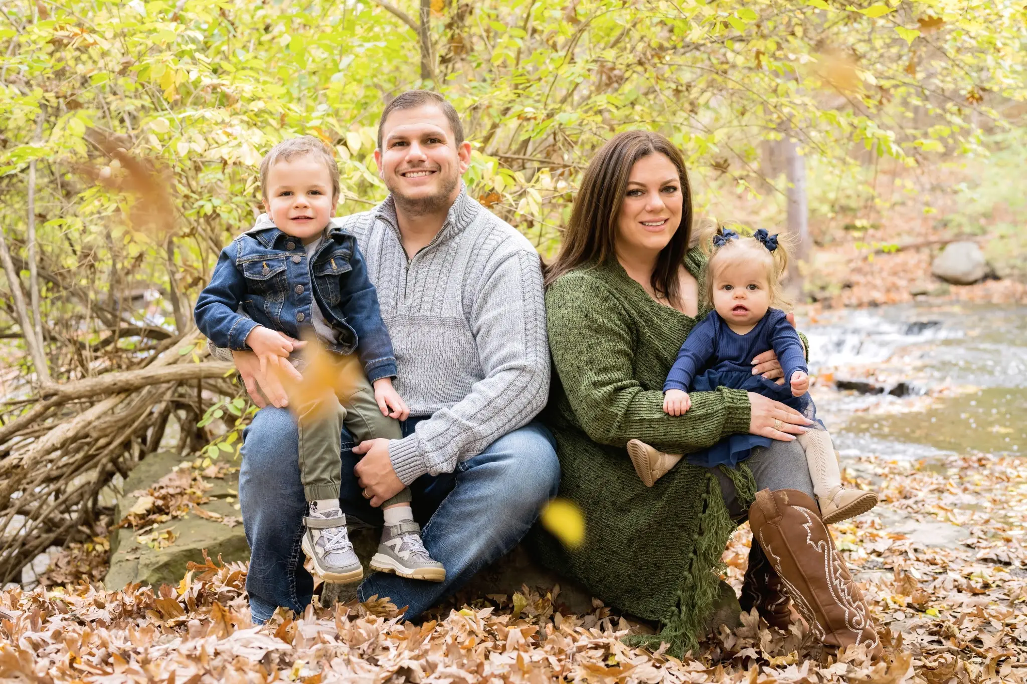 A family of four sitting on autumn leaves in a forest.