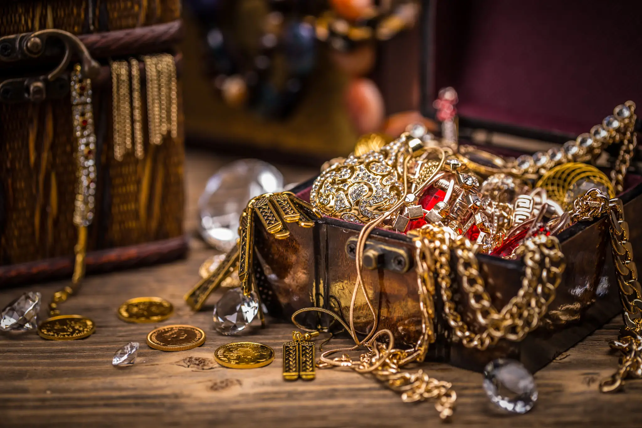 Gold necklaces, chains, coins, and gemstone jewelry spilling from an antique chest, showcasing precious metals and valuables.